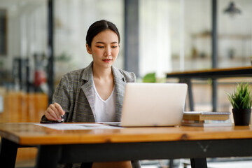 Fototapeta premium Portrait of beautiful asian young Business woman working audit and calculating expense annual financial report balance sheet statement,doing finance making notes on paper graph data checking document.