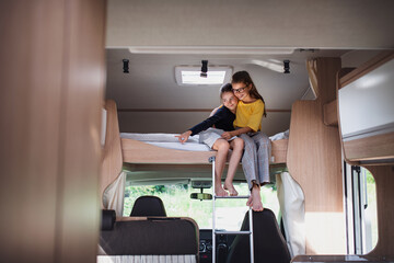 Small girls sisters sittining on bed indoors in caravan, family holiday trip. - obrazy, fototapety, plakaty