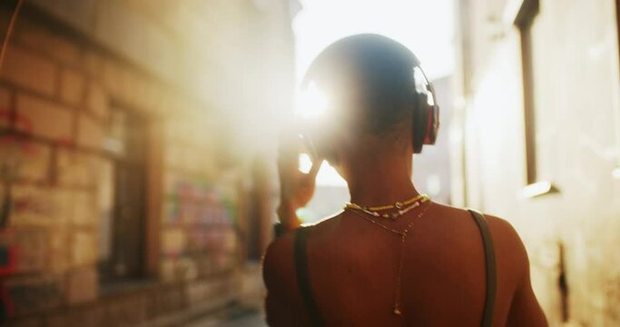 Active cheerful young african woman wearing headphones and listening favorite music outside. Black stylish girl dancing on modern hipster street downtown. Sunny day. People and emotions.