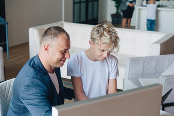 Obraz premium Dad and his teenage son are working at the computer. Online communication. Teacher and pupil. Tutor.