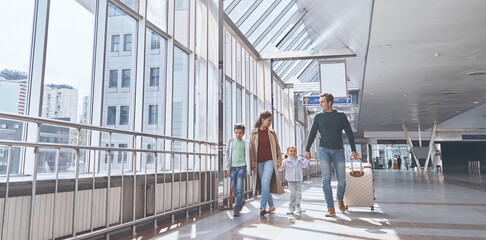 Full length of happy family with two little kids walking by airport terminal