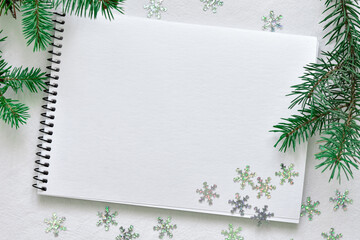 mock-up from a watercolor white sketchbook and shiny snowflakes on a black spring lying on a linen tablecloth with sprigs of a green Christmas tree
