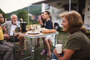 Familie mit mehreren Generationen sitzt und isst im Freien mit dem Auto, Urlaubsreise mit dem Wohnwagen.