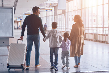 Full length rear view of family with two little kids walking by airport terminal