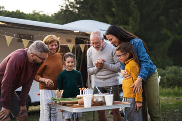 Senior man celebrating birthday outdoors at campsite, multi-generation family caravan holiday trip.