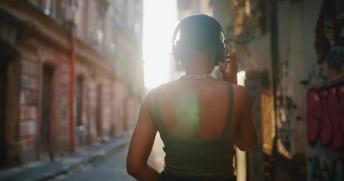 Young satisfied cheerful african american woman wearing black headphones and listening favorite music. Dancing girl in modern street. Emotions, people and fashion.