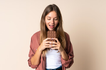 Young Lithuanian woman isolated on beige background eating a chocolate tablet