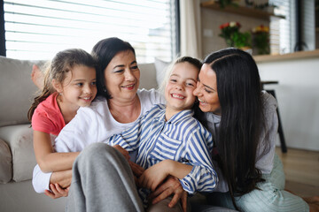 Happy small girls with mother and grandmother indoors at home, hugging.