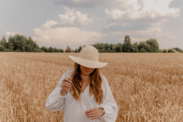 young woman plus size model in long white drees on field of ripe cereals and a blue sky with clouds in autumn, a concept of harvest, agribusiness and farming