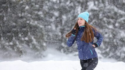 Fototapeta na wymiar Young pretty woman jogging in winter park. Outdoors cold weather running lifestyle background with copy space