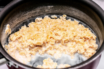 on the stove, a healthy and dietary oatmeal porridge with milk is prepared in a burgundy non-stick ladle