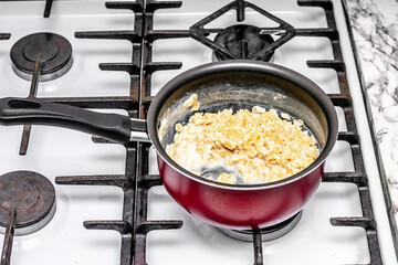 on the stove, a healthy and dietary oatmeal porridge with milk is prepared in a burgundy non-stick ladle