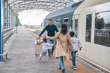 Full length of happy woman and two little kids meeting father on railroad station platform - obrazy, fototapety, plakaty