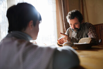 Rear view of poor small girl with father eating indoors at home, poverty concept.