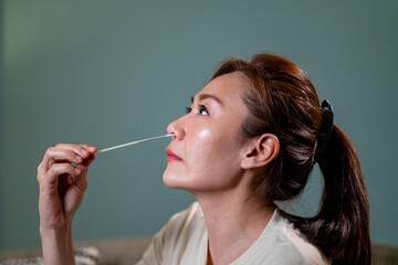 Obraz premium Asian woman using rapid antigen test kit for self test COVID-19 epidemic at home. Adult female unpacking a swab for inserts into her nose. COVID-19 coronavirus pandemic protection concept.