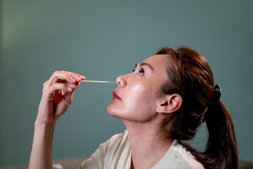 Fototapeta premium Asian woman using rapid antigen test kit for self test COVID-19 epidemic at home. Adult female unpacking a swab for inserts into her nose. COVID-19 coronavirus pandemic protection concept.