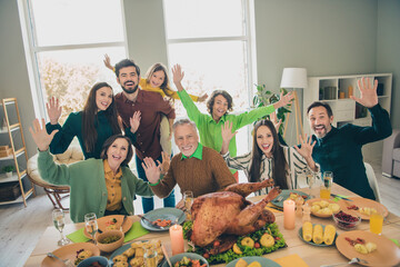 Photo of cute friendly family eating holiday turkey smiling sitting table waving arms hello hi indoors house room
