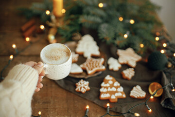 Hand holding warm coffee cup on background of christmas gingerbread cookies, fir branches, warm...