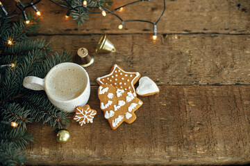 Christmas gingerbread cookies, coffee cup, fir branches on  background of warm lights bokeh on...