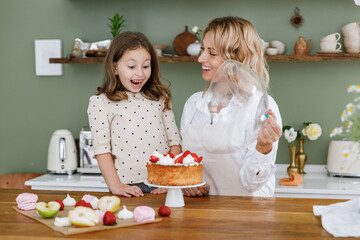 Happy chef cook baker mom woman in white shirt work with child baby girl helper removes lid from...