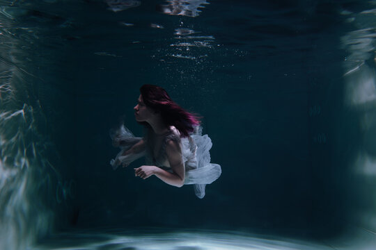 Photo of a beautiful girl with red hair posing in the water. She looks like a mermaid
