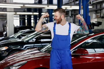 Strong young male professional technician car mechanic man in denim blue overalls white t-shirt...