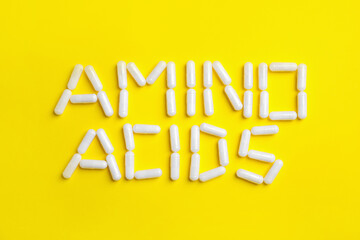 Phrase Amino acids made of pills on yellow background, flat lay