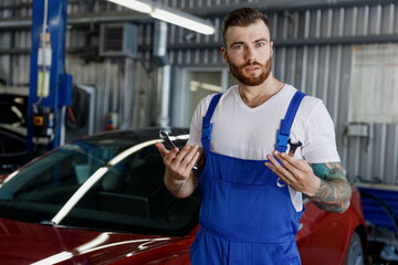 Confused young professional technician car mechanic repairman man wear denim blue overalls white...