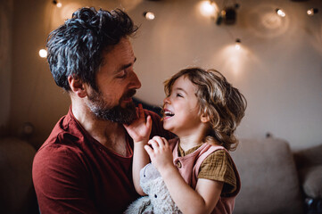 Mature father with small daughter standing indoors at home, holding and hugging. - obrazy, fototapety, plakaty