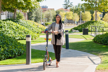 Front view of an adult muslim woman looking at camera with an electric scooter in the park