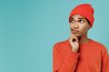 Young minded pensive thoughtful uncertain african american man 20s wear red shirt hat prop up chin look aside isolated on plain pastel light blue background studio portrait. People lifestyle concept