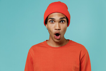 Young surprised shocked amazed african american man 20s in red shirt hat look camera with opened mouth say wow isolated on plain pastel light blue background studio portrait. People lifestyle concept.