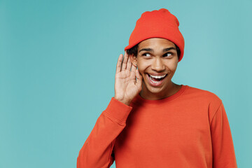 Young curious nosy smiling african american man in red shirt hat try to hear you overhear listening...
