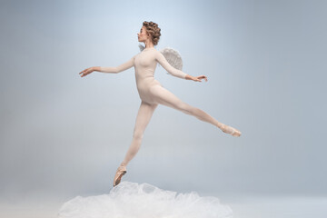 Young and graceful ballet dancer, ballerina dancing in image of angel with wings isolated on gray studio background. Art, motion, action, flexibility, inspiration concept.