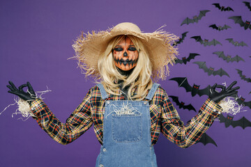 Young woman with Halloween makeup mask wears straw hat scarecrow costume hold hand in yoga om...