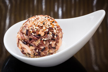 Japanese Salmon Rice ball with multi-grain rice and furikake sesame seasoning on a minimalist white spoon and striped background. 