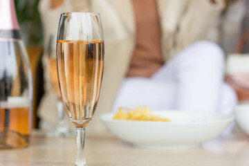 Closeup on sparkling rose wine glass with snacks bowl and woman on background. Friends meeting, party celebration concepts