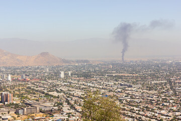 Flat city views of Santiago with fire smoke on background. Sunny day on polluted capital of Chile....