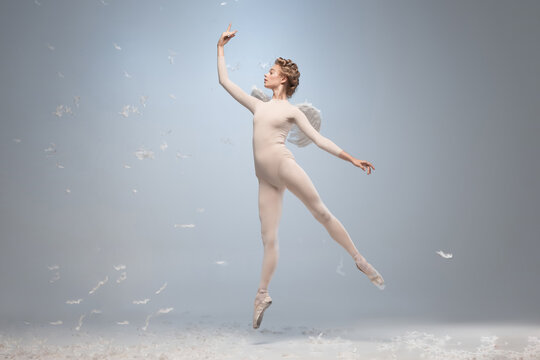 Full-length portrait of beautiful graceful ballerina dancing in image of angel with wings isolated on gray studio background. Art, motion, action, flexibility, inspiration concept.
