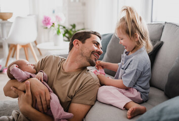 Fototapeta premium Happy young man taking care of his newborn baby and little daughter indoors at home, paternity leave.