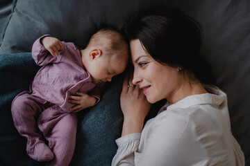 Top view of happy young mother with her newborn baby girl lying on sofa indoors at home.