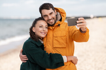 technology, relationships and people concept - happy couple with smartphone on autumn beach