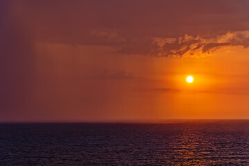 Fototapeta na wymiar Sunset and rain at sea in the same photo. Sunlight and rainy clouds in the horizon at sea.