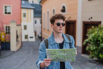 Happy young man tourist outdoors on trip in town, using map.