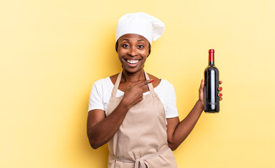 black afro chef woman looking excited and surprised pointing to the side and upwards to copy space. wine bottle concept