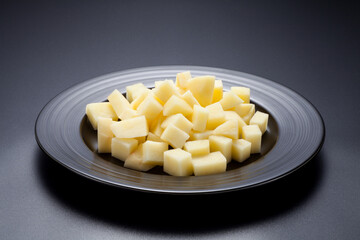 Chopped raw potatoes in a black plate on black background.