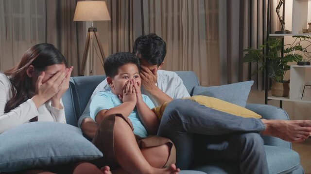 Asian Family, Leisure And People Concept, Father, Mother And Little Son Watching Scary Movie On Tv At Home
