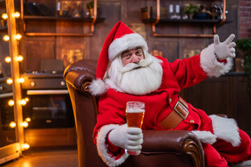 Portrait of santa claus sitting on a leather sofa and drinking beer for christmas