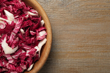 Cut radicchio in bowl on wooden table, top view. Space for text
