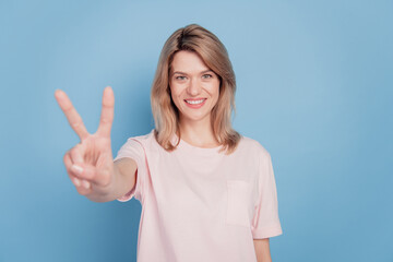 Fototapeta premium Portrait of charming positive girl fingers demonstrate v-sign white smile on blue background